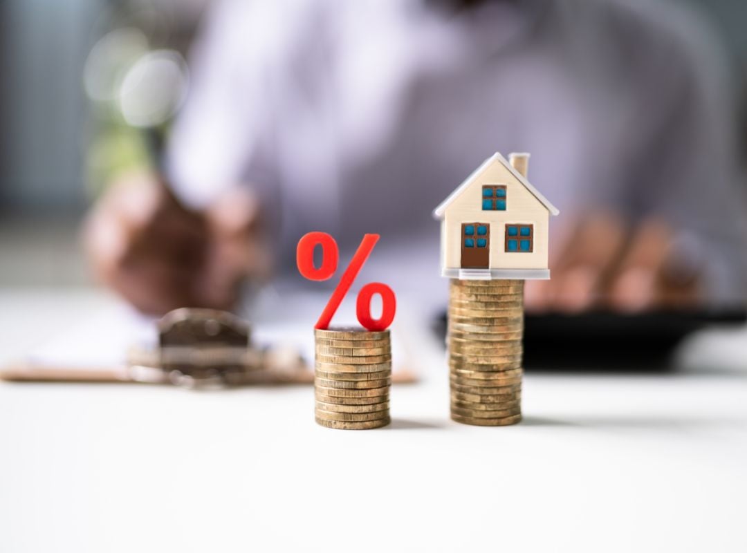 Häuschen und Prozent-Zeichen stehen auf zwei Geldstapel. Festzins vs. variabler Zins: Was ist besser für Ihre Immobilie in der Schweiz?
