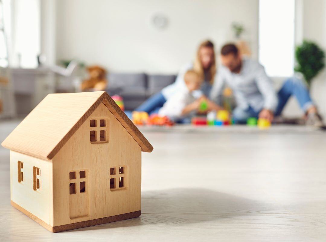 Modellhaus auf dem Tisch mit Familie im Hintergrund, die im Wohnzimmer spielt.