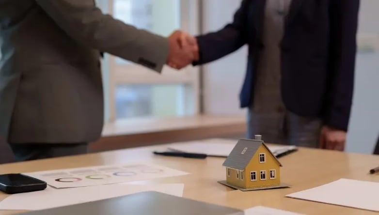Handschlag bei Immobilien-Onboarding mit Miniaturhaus auf dem Tisch