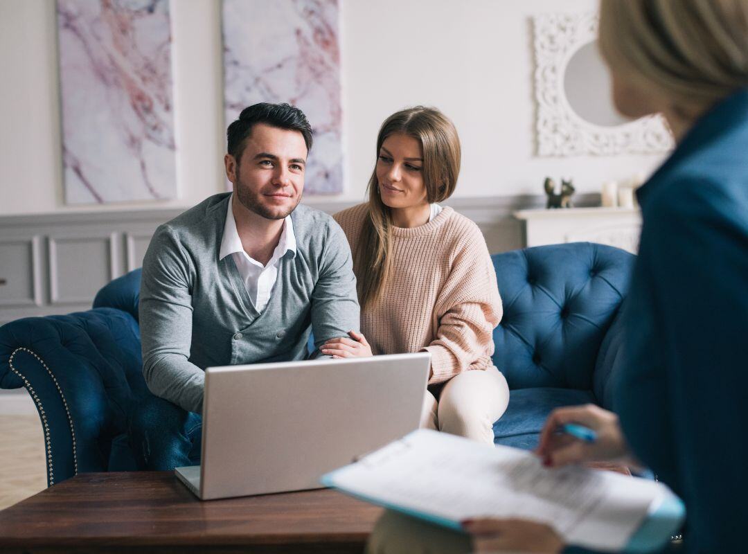 Paar sitzt auf der Couch und wird von Experten beraten. Stockwerkeigentum Versicherung.