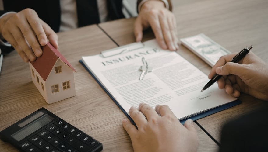 Unterzeichnung eines Vertrags neben Hausmodell und Taschenrechner